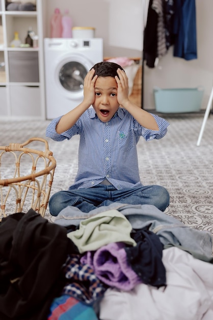 Un bambino con i capelli scuri è seduto sul pavimento della lavanderia in bagno