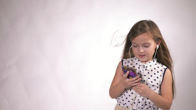 Child with earflaps dancing at studio background The girl listens to music on the smartphone