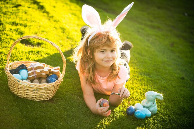 Child with easter eggs and bunny ears laying on grass Funny boy easter bunny kids Happy Easter kids face