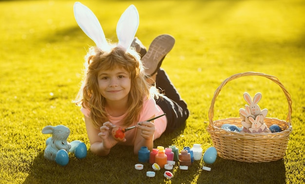 Child with easter eggs and bunny ears laying on grass painting eggs happy easter kids face