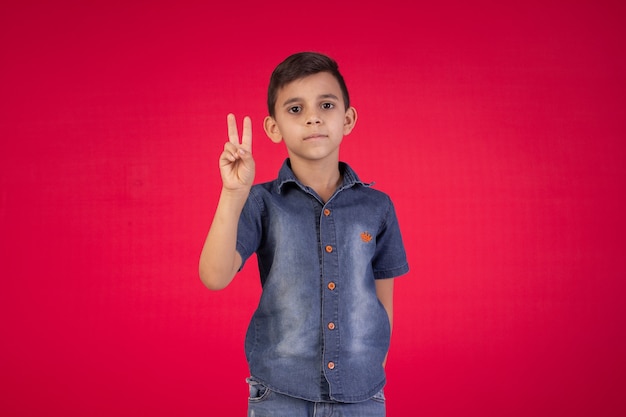 Child with facial expressions in a studio photo on red background.