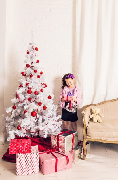 Ребенок с подарочной коробкой возле белой елки