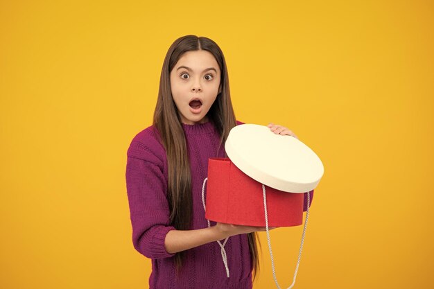 Child with gift present box on isolated yellow background Presents for birthday Valentines day New Year or Christmas Surprised emotions of young teenager girl