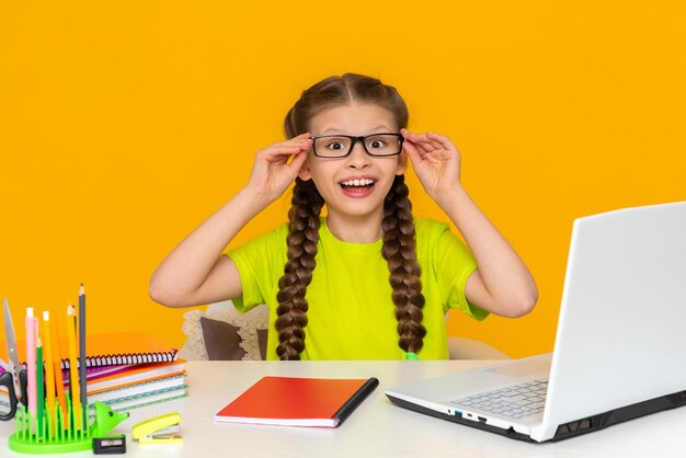 A child with glasses is sitting at a desk a happy little girl is sitting at her laptop childrens school distance education online