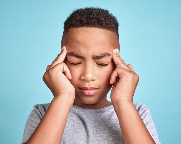 Child with headache stress and mental health problem or fatigue pain on blue studio background Frustrated african american kid depressed boy and angry youth with fingers massaging temples of head