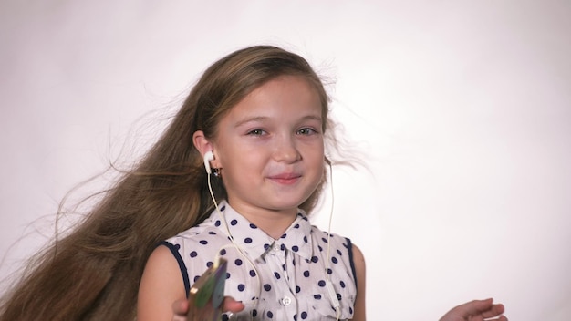 Photo child with headphones dancing at studio background girl listens to music on smartphone beautiful cute happy little girl listens to music