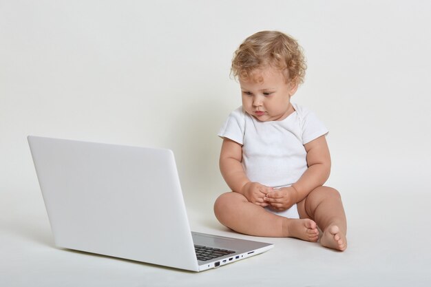 Child with lap top computer sitting on floor isolated over white wall