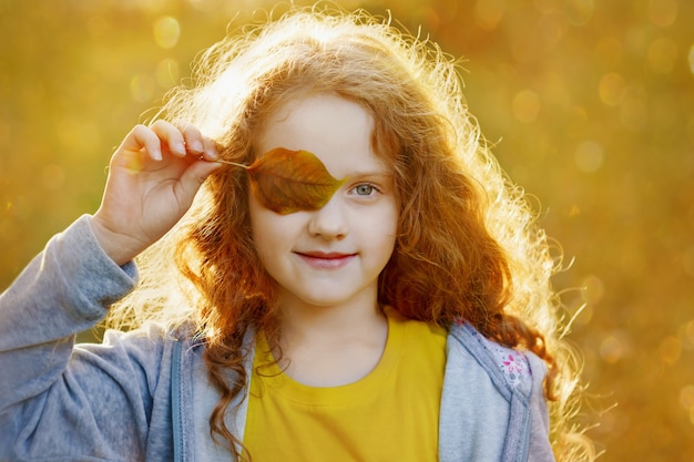 Child with leaves eyes, resting in golden autumn park.