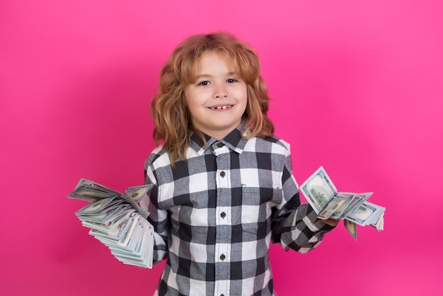 Фото Ребенок с большим количеством банкнот в долларах, изолированных на розово-красном фоне студии