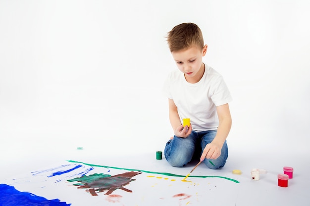 絵筆を持つ子供。 9歳の少年、モダンな髪型、白いシャツ、ブルージーンズは、分離されたペイントブラシを描画しています。