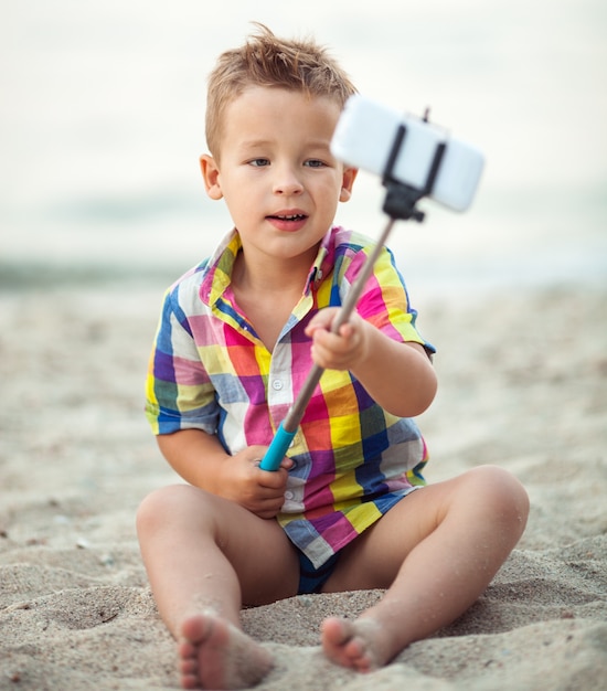 Photo child with phone and selfie stick on the beach