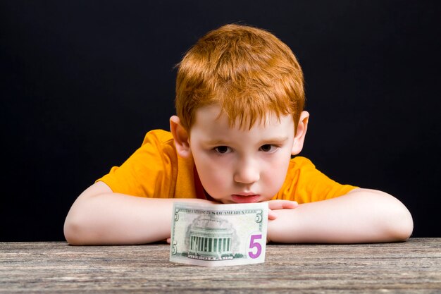 Child with red hair, close-up portrait of a beautiful boy with American dollars, cash available for a small child