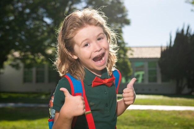 Child with rucksacks in the school park excited pupil with backpacks outdoors thumbs up ok