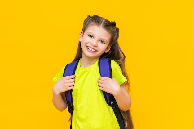 책가방을 메고 있는 아이 중학교 및 중등학교를 위한 교육 과정 매력적인 어린 소녀가 노란색 외진 배경에서 학교에 가고 있습니다