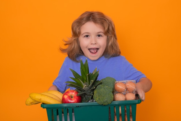 Ребенок с корзиной для покупок возбужденный ребенок выбирает еду в магазине или продуктовом магазине