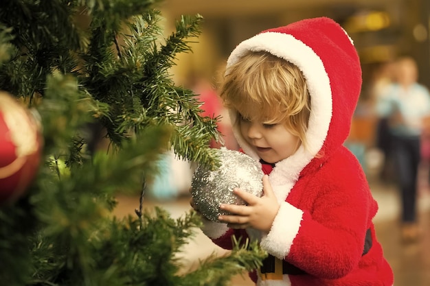 Bambino con palla d'argento sull'albero di natale che indossa il costume da babbo natale