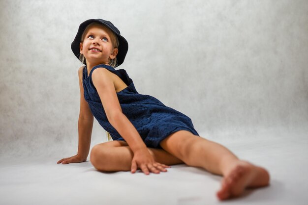 Child with a smile in a hat and a blue dress poses in the studio