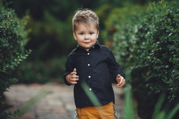 Foto bambino con un sorriso che cammina nel parco su uno sfondo di alberi verdi