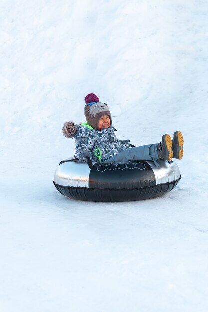 Child with snow tubing winter activity, slide from snow hill