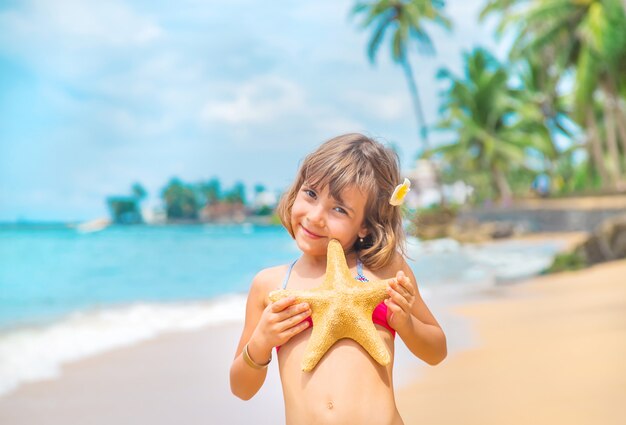 A child with a starfish in his hands on the beach.