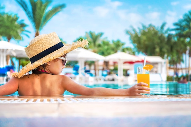 Child with a straw hat and a cocktail by the pool