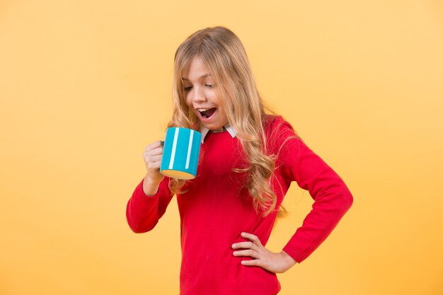 Child with surprised face hold blue cup on orange background