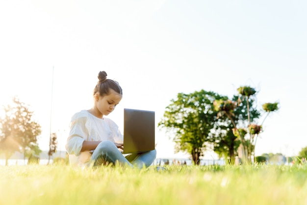 屋外でタブレットPCを持つ子供。コンピューターと草の上の少女