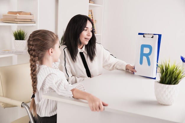 Child with therapist working on pronunciation and sounds together sitting in the class.