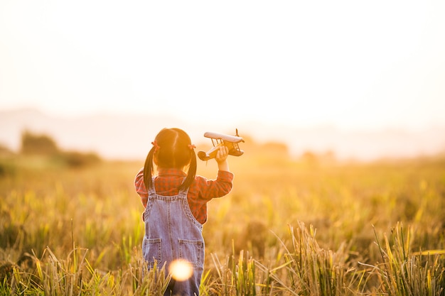 Child with toy airplane in nature at sunset