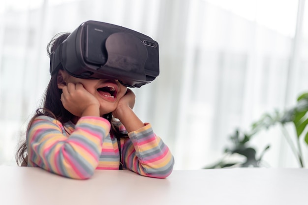 Child with virtual reality headset sitting behind table indoors at home