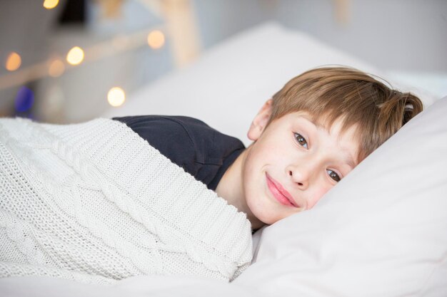 Ребенок проснулся Мальчик лежит на подушке накрытой одеялом