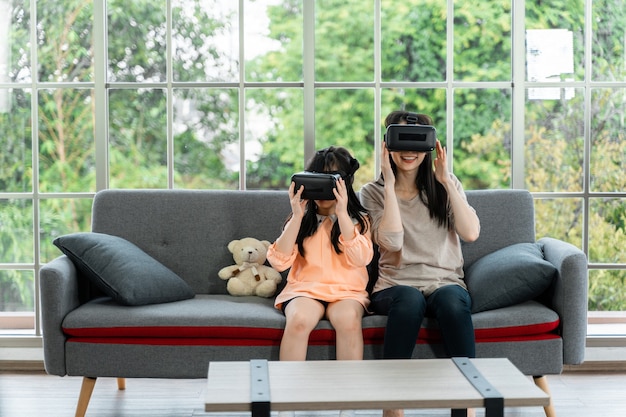 Child and woman with virtual reality headset smiling while sitting on sofa indoors at home