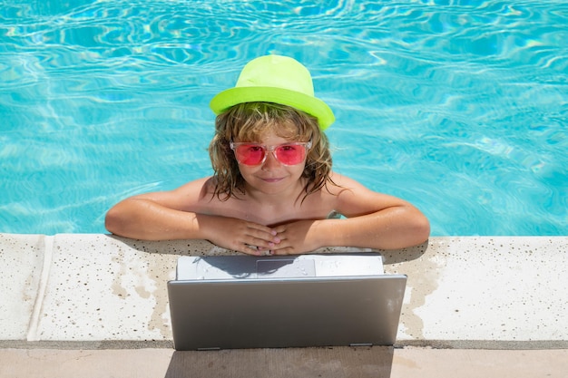 Child working on laptop computer at swimming pool Summer online technology Traveler relaxing on tropical water in summer holidays vacation Travel trip kid using laptop