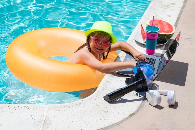 Child working on laptop computer at swimming pool Summer online technology Traveler relaxing on tropical water in summer holidays vacation Travel trip kid using laptop