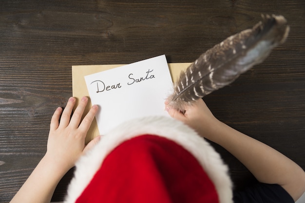 Il bambino scrive la lettera a santa nel cappello di babbo natale ... concetto di natale