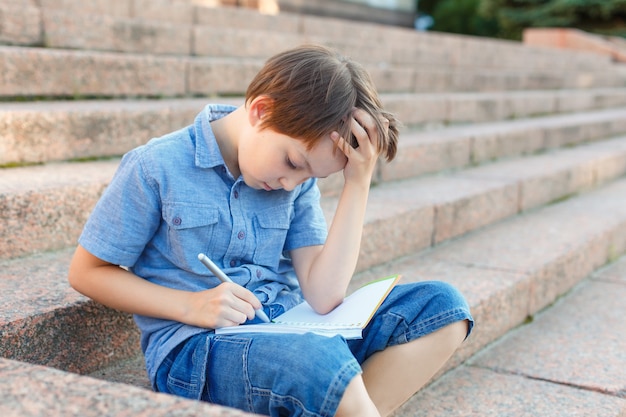 Bambino che scrive in un taccuino. scolaro del preteen che fa i compiti.