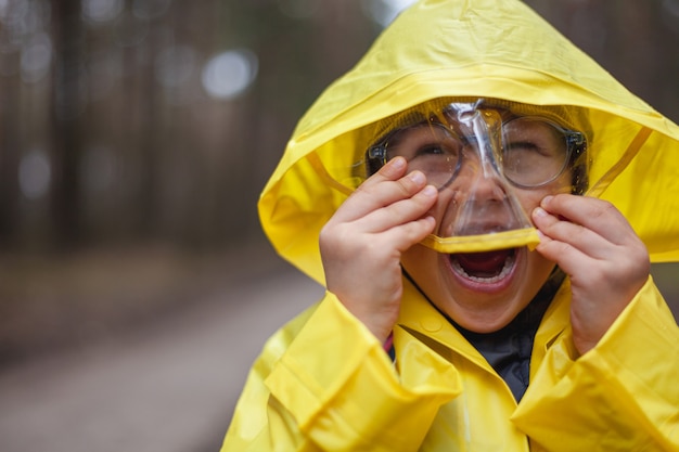 Child in a yellow raincoat walking in the forest after the rain, laughing and fun, look at camera