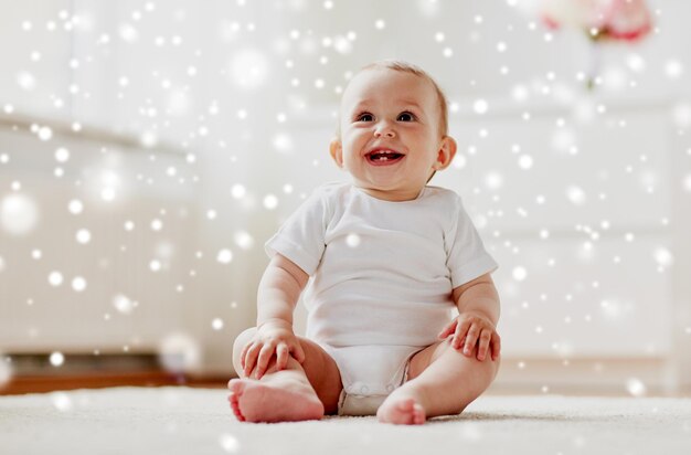 Photo childhood babyhood and people concept happy little baby boy or girl sitting on floor at home over snow