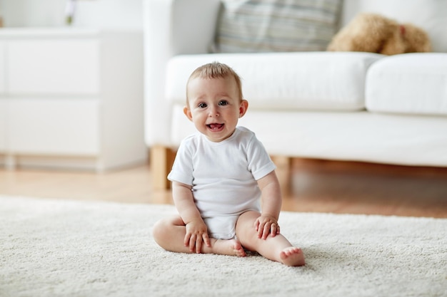 Photo childhood, babyhood and people concept - happy little baby boy or girl sitting on floor at home