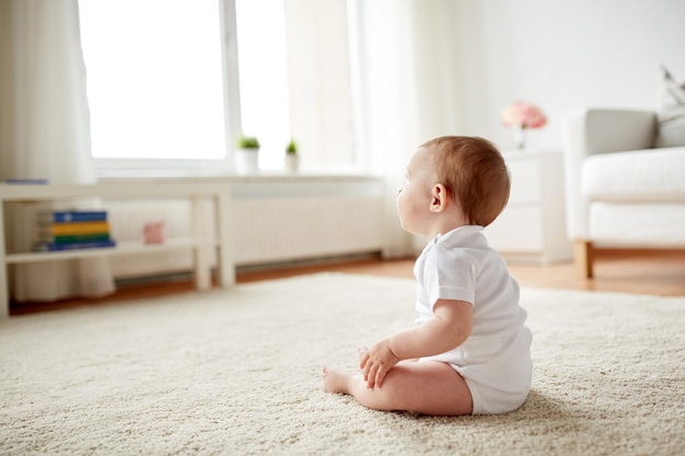 Photo childhood, babyhood and people concept - happy little baby boy or girl sitting on floor at home