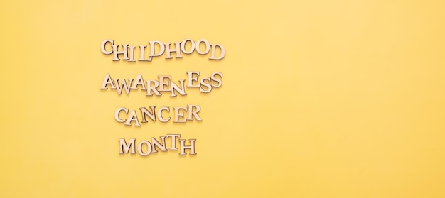 Photo childhood cancer awareness month text from wooden letters on yellow background with copy space