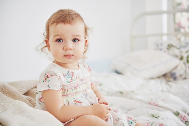 Childhood concept. baby girl in cute dress siting at bed playing with toys by the home. White vintage childroom