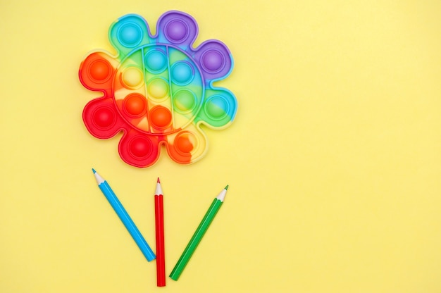 Childhood concept Rainbow color toy anti stress for fingers Pop It in the shape of a flower on a yellow background