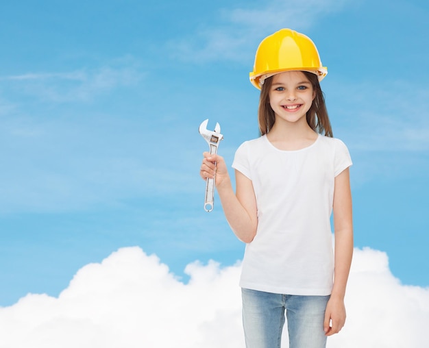 childhood, construction and people concept - smiling little girl in protective helmet with wrench