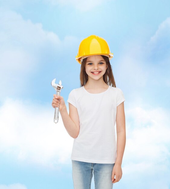 childhood, construction and people concept - smiling little girl in protective helmet with wrench