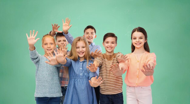 childhood, education, friendship, gesture and people concept - happy smiling children waving hands over green school chalk board background