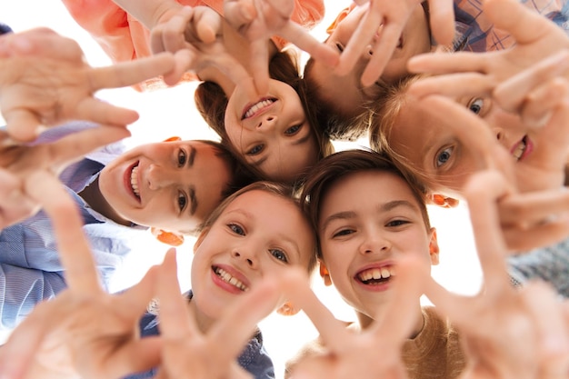 childhood, fashion, friendship and people concept - happy smiling children showing peace hand sign and standing in circle