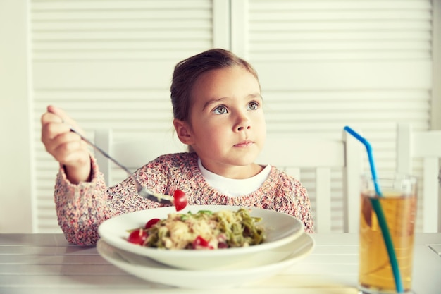 childhood, food and people concept - little girl eating pasta for dinner at restaurant or cafe