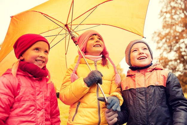 childhood, friendship, season, weather and people concept - group of happy kids with umbrella in autumn park