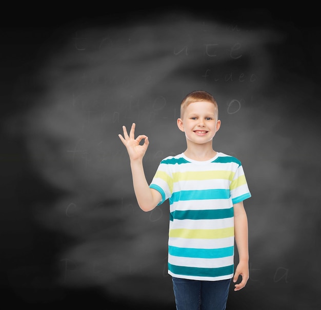 childhood, gesture, education and people concept - smiling little boy in casual clothes making ok gesture over blackboard background